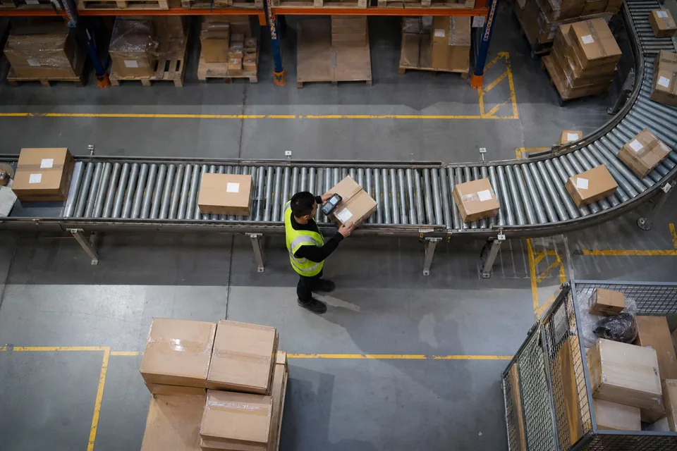 Top-down view of an ecommerce warehouse with parcels on conveyor belts and a worker scanning a box