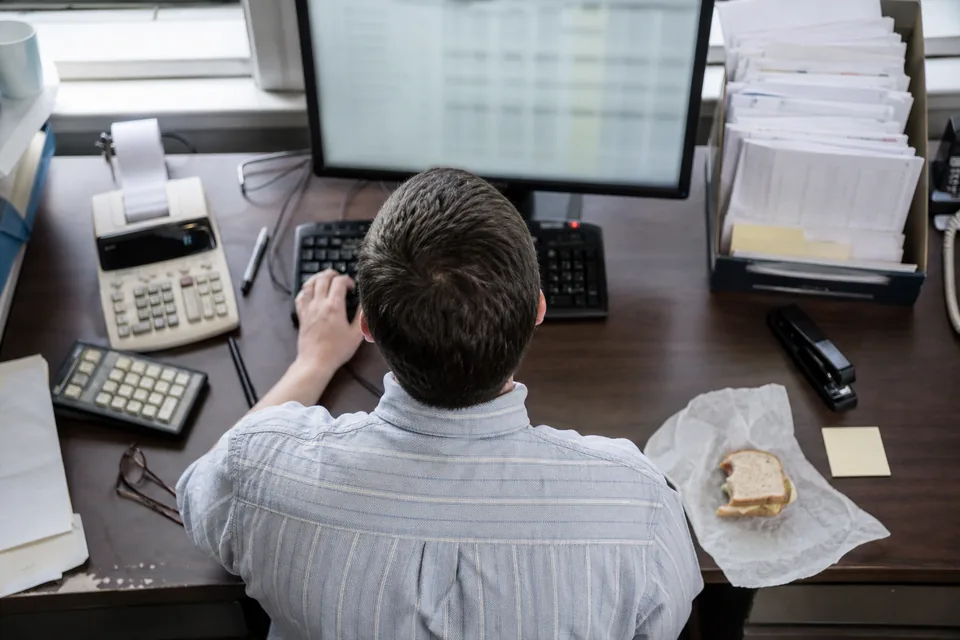 Overhead view of an accountant's desk with monitor, calculator, invoice tray and keyboard