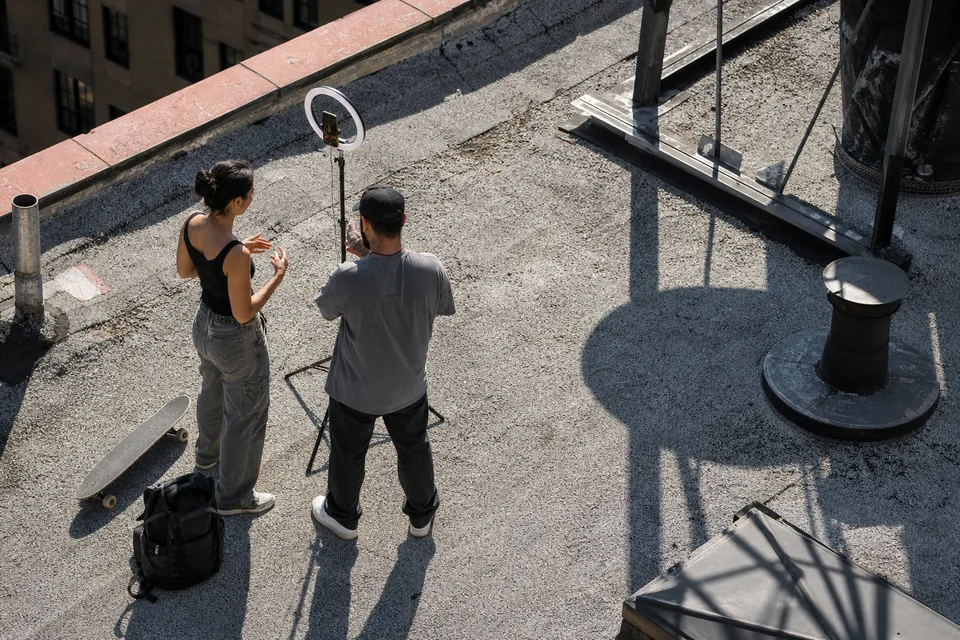 Drone view down on a rooftop where two adults film a short vertical video on a phone with a ring light